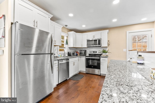 kitchen with recessed lighting, stainless steel appliances, white cabinetry, light stone countertops, and dark wood finished floors