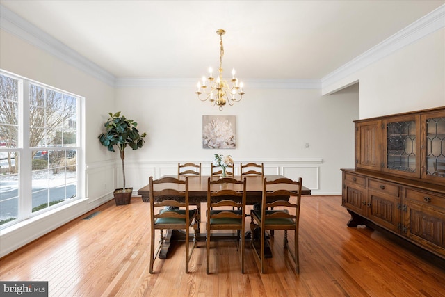 dining area featuring light wood finished floors, wainscoting, visible vents, and crown molding