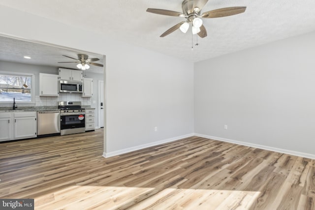 interior space featuring sink, stainless steel appliances, light hardwood / wood-style floors, white cabinets, and decorative backsplash