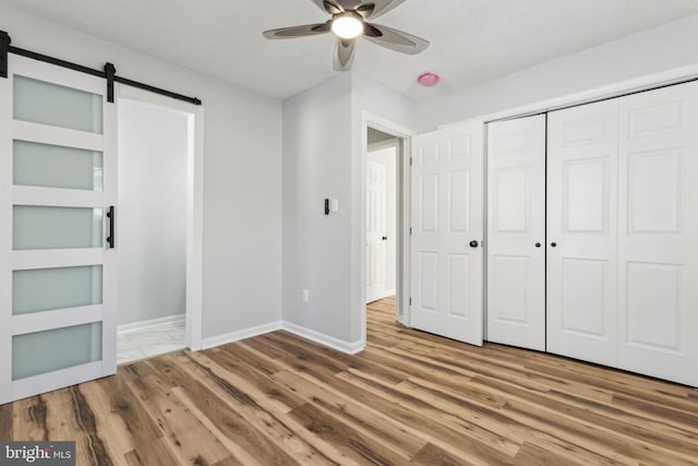 unfurnished bedroom with hardwood / wood-style flooring, a barn door, ceiling fan, and a closet