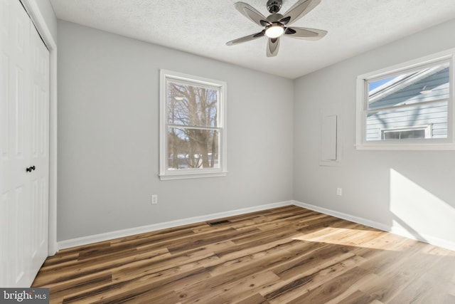 unfurnished bedroom with multiple windows, hardwood / wood-style flooring, a textured ceiling, and a closet