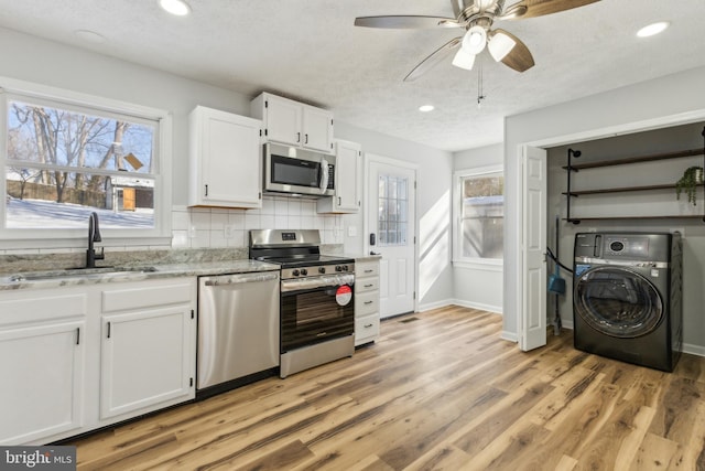 kitchen with sink, appliances with stainless steel finishes, white cabinetry, tasteful backsplash, and washer / dryer