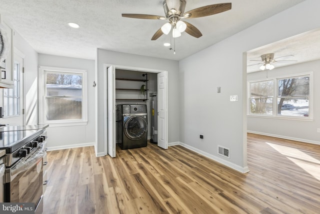 interior space with washer / clothes dryer, electric range, ceiling fan, a textured ceiling, and light hardwood / wood-style flooring