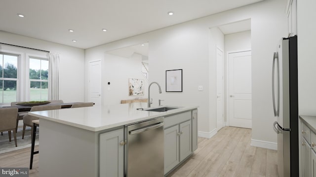 kitchen with a kitchen bar, sink, light hardwood / wood-style flooring, appliances with stainless steel finishes, and a kitchen island with sink