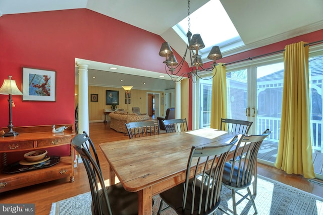 dining area with crown molding, a notable chandelier, wood finished floors, high vaulted ceiling, and ornate columns