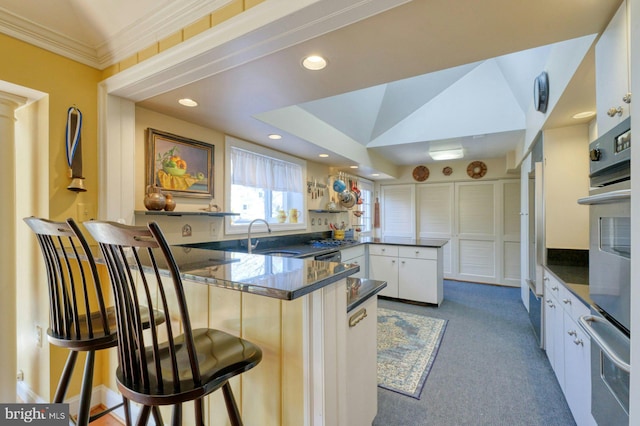 kitchen with carpet, dark countertops, white cabinetry, a peninsula, and a kitchen breakfast bar