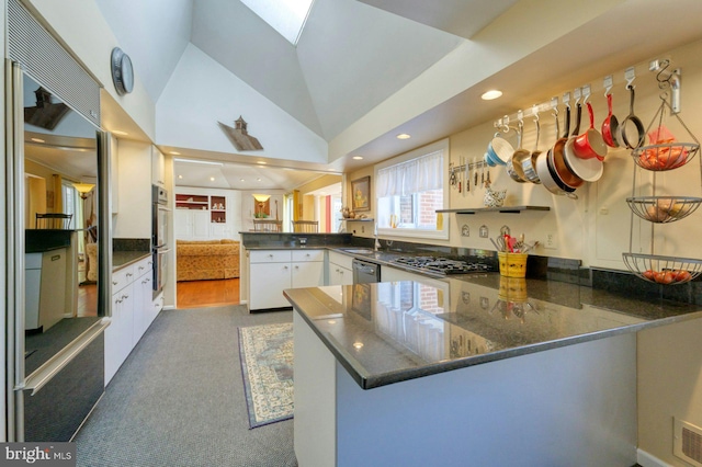 kitchen with a peninsula, a skylight, appliances with stainless steel finishes, and white cabinets