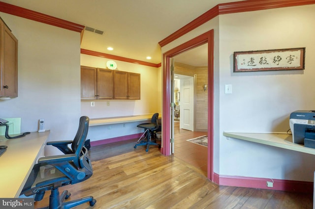 office area with visible vents, baseboards, light wood-style floors, built in desk, and crown molding