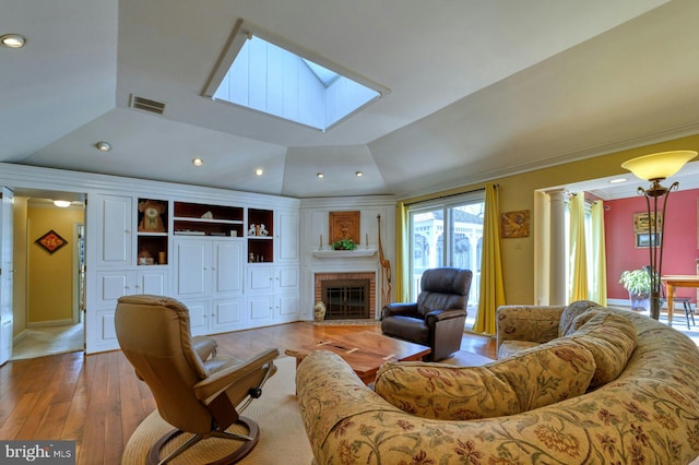 living area with vaulted ceiling with skylight, decorative columns, visible vents, light wood-type flooring, and a fireplace