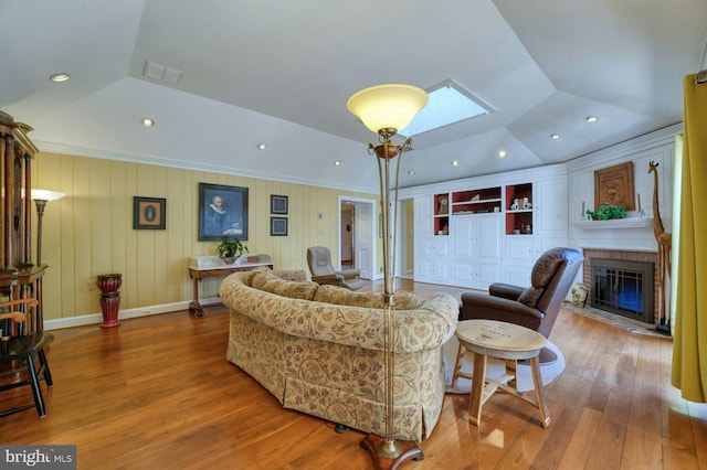 living room featuring lofted ceiling with skylight, a brick fireplace, visible vents, and wood finished floors