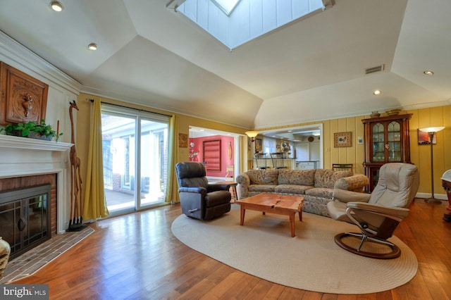 living area featuring vaulted ceiling with skylight, visible vents, wood finished floors, a fireplace, and recessed lighting