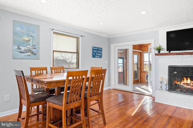 dining area with crown molding, a healthy amount of sunlight, a fireplace, and wood-type flooring