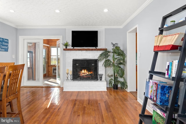 living room featuring crown molding, hardwood / wood-style floors, a brick fireplace, and a textured ceiling