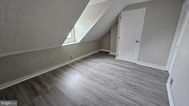 additional living space with lofted ceiling, light hardwood / wood-style flooring, and a textured ceiling