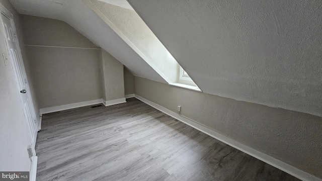 additional living space with wood-type flooring, lofted ceiling, and a textured ceiling