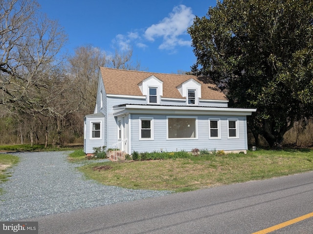 view of front facade with a front yard, entry steps, gravel driveway, and roof with shingles