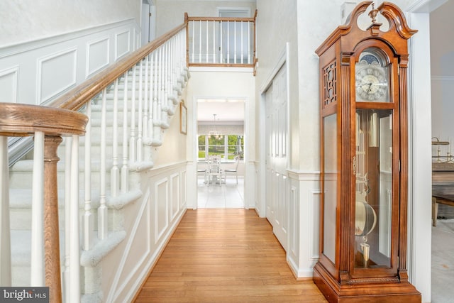 corridor with a towering ceiling, wainscoting, stairway, a decorative wall, and light wood-style flooring