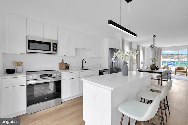 kitchen featuring white cabinetry, stainless steel appliances, decorative light fixtures, and sink