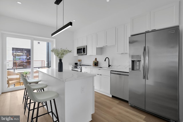 kitchen with pendant lighting, sink, appliances with stainless steel finishes, white cabinetry, and a center island