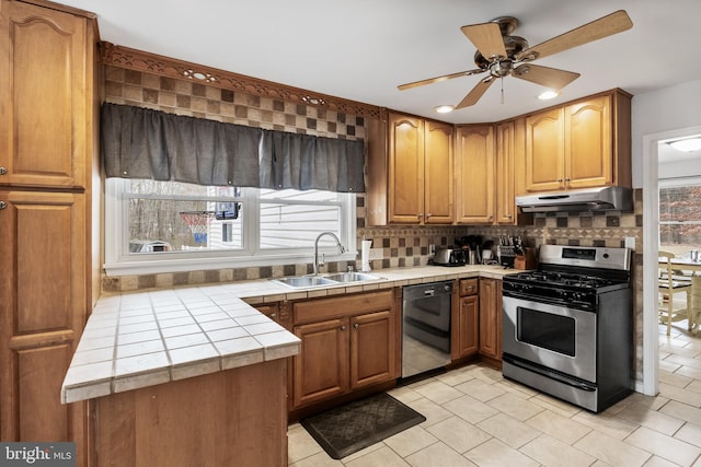 kitchen with dishwasher, tile countertops, under cabinet range hood, stainless steel range with gas cooktop, and a sink