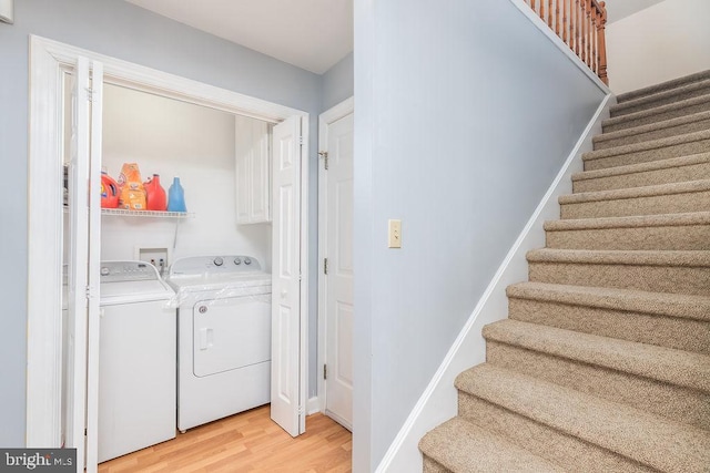 laundry room featuring washing machine and dryer, cabinet space, baseboards, and wood finished floors