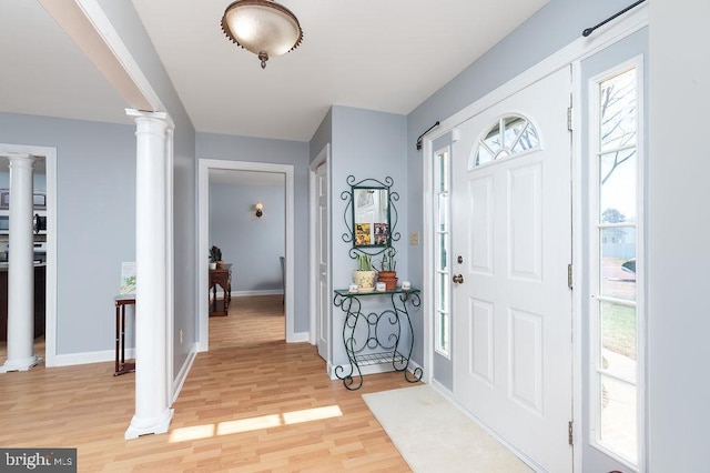 foyer entrance featuring baseboards, decorative columns, and light wood finished floors