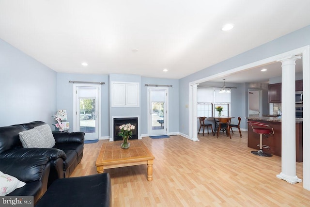 living room with a wealth of natural light, light wood-style flooring, and ornate columns