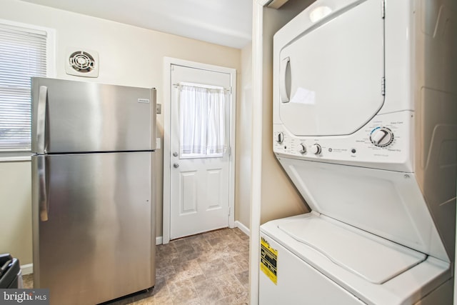 laundry area with laundry area, visible vents, baseboards, stacked washer and clothes dryer, and stone finish flooring