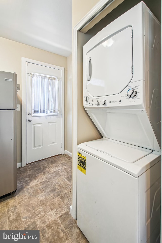 washroom with laundry area, stone finish flooring, baseboards, and stacked washer / dryer