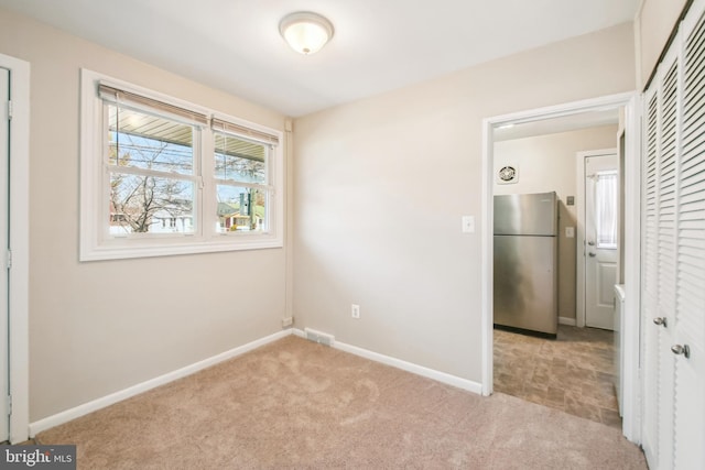 unfurnished bedroom with light carpet, visible vents, baseboards, a closet, and freestanding refrigerator