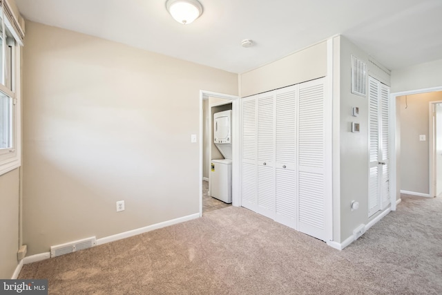 unfurnished bedroom with light carpet, stacked washer and dryer, visible vents, baseboards, and a closet