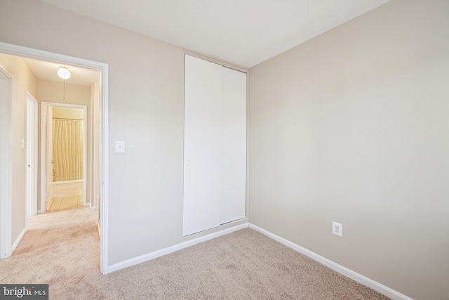 unfurnished bedroom with baseboards, a closet, attic access, and light colored carpet