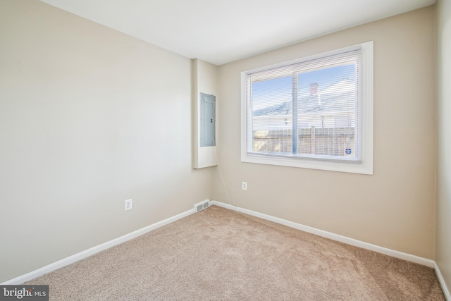 empty room with electric panel, light carpet, visible vents, and baseboards