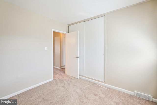 unfurnished bedroom with a closet, visible vents, light carpet, and baseboards