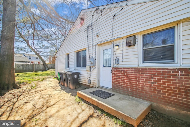 view of exterior entry with brick siding, fence, and a patio