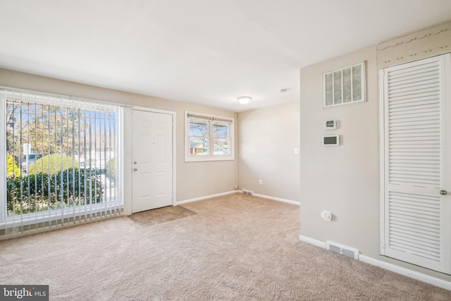 foyer entrance featuring light carpet, visible vents, and baseboards