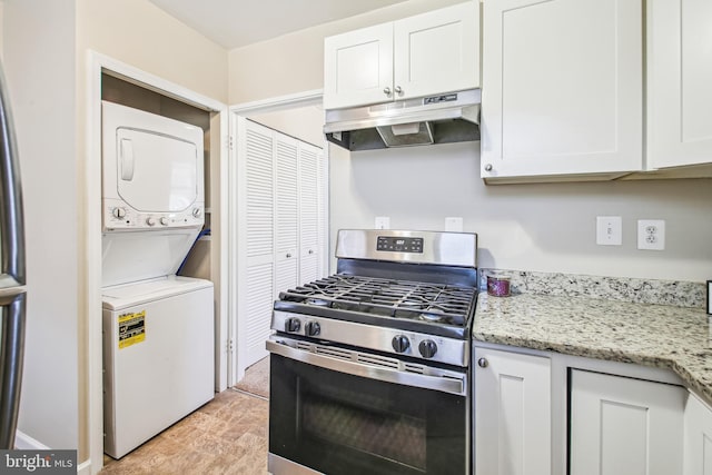 kitchen with under cabinet range hood, stacked washer / dryer, white cabinets, light stone countertops, and gas range