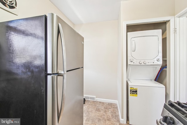 clothes washing area featuring visible vents, laundry area, stacked washer and clothes dryer, and baseboards