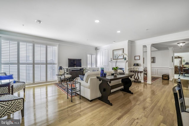 living area with a decorative wall, light wood-style floors, wainscoting, ornate columns, and crown molding