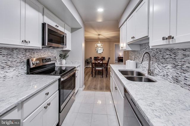 kitchen featuring pendant lighting, sink, white cabinets, stainless steel appliances, and light stone countertops