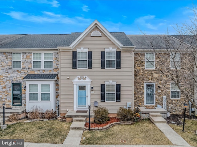 multi unit property with stone siding, a shingled roof, and a front lawn