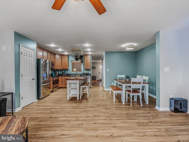 kitchen featuring brown cabinetry, dark countertops, light wood-style flooring, appliances with stainless steel finishes, and a kitchen breakfast bar