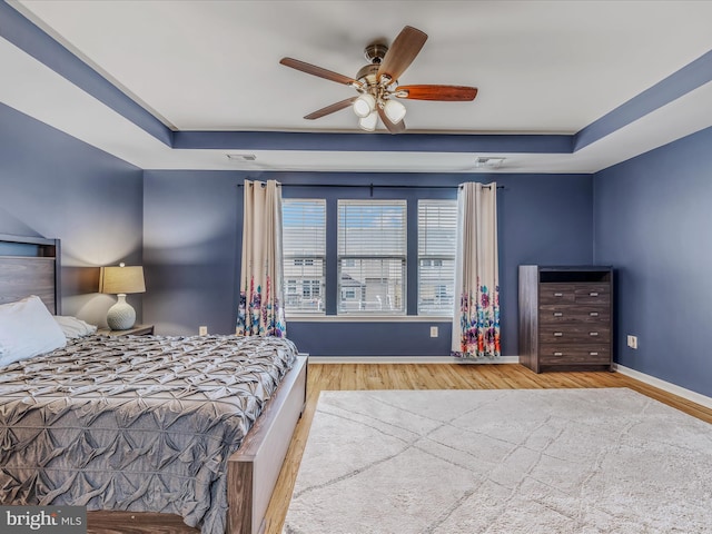 bedroom featuring visible vents, a ceiling fan, baseboards, light wood-type flooring, and a raised ceiling