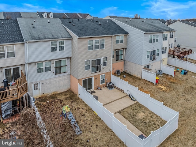 back of house featuring a fenced backyard, a residential view, central AC, and brick siding