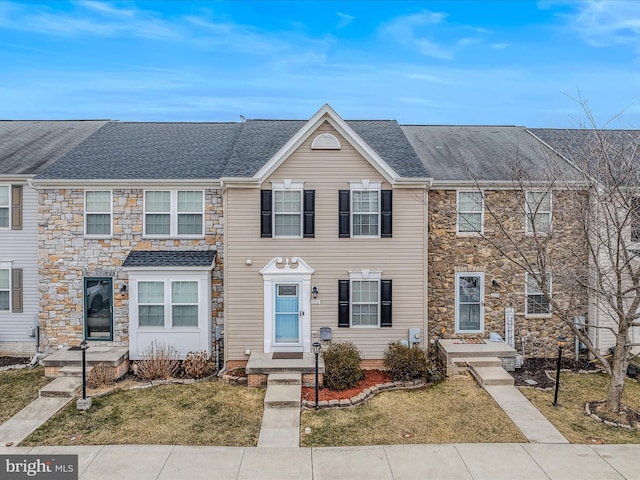 multi unit property with a front yard, stone siding, and roof with shingles