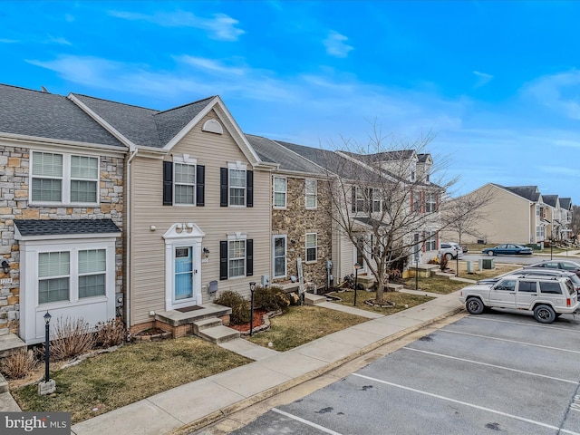 multi unit property with uncovered parking, a shingled roof, and a residential view