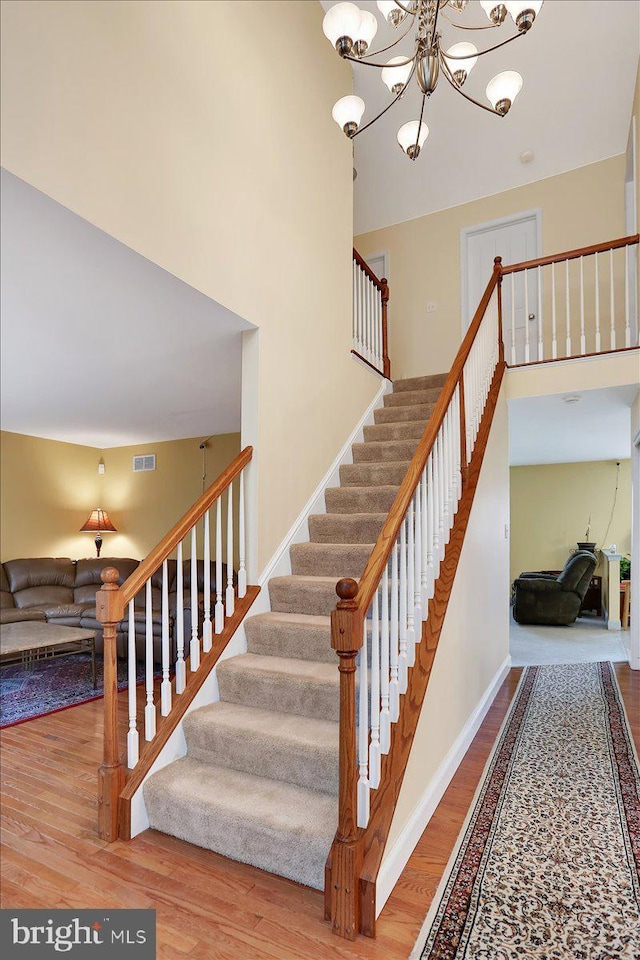 staircase featuring a towering ceiling, wood-type flooring, and a notable chandelier