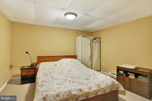 bedroom with a drop ceiling, a baseboard heating unit, and carpet flooring