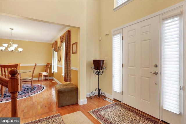 entryway with an inviting chandelier, plenty of natural light, crown molding, and light hardwood / wood-style flooring