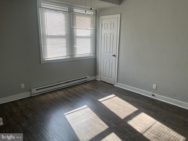 spare room featuring baseboard heating and dark hardwood / wood-style floors